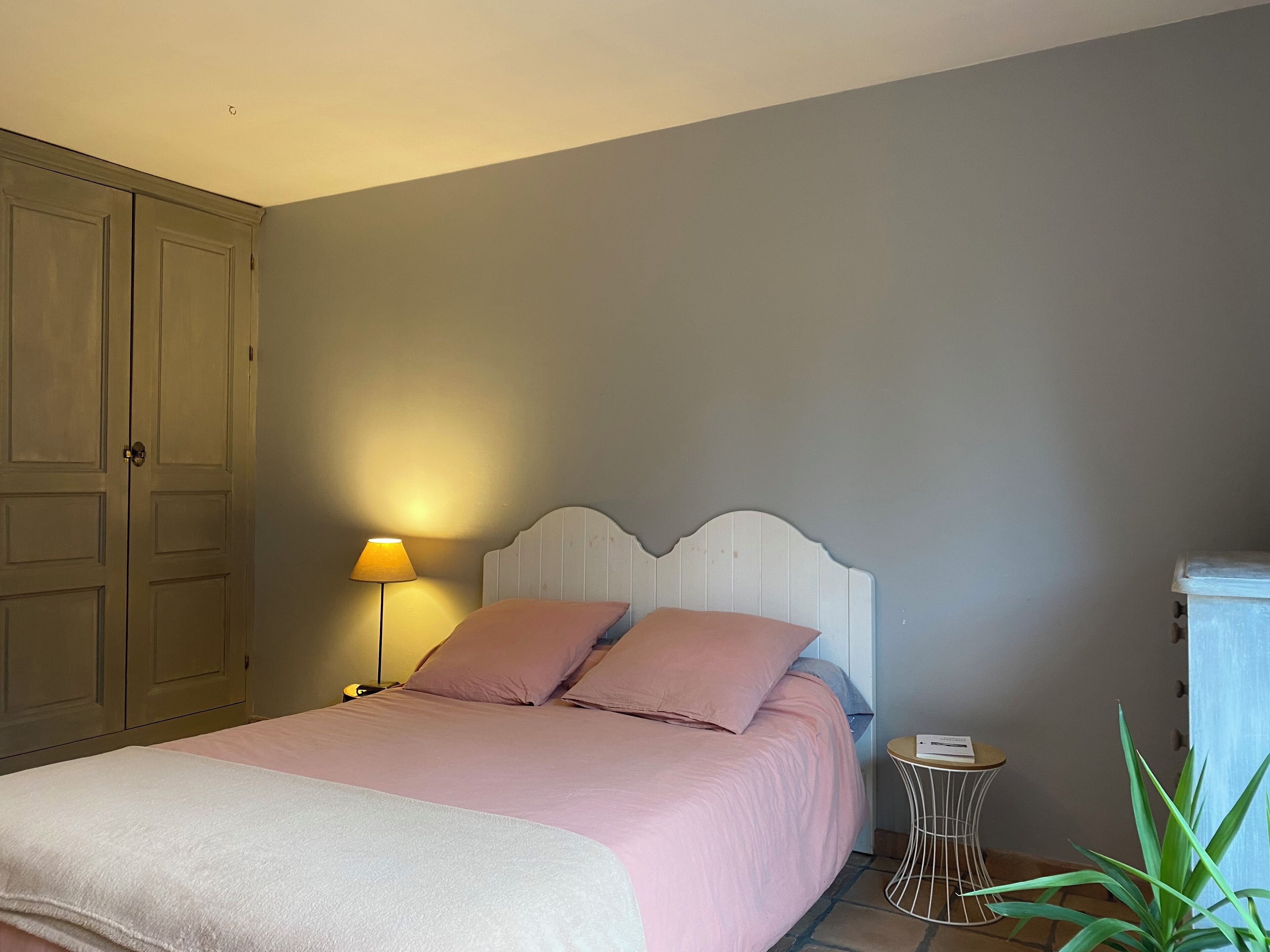 Une chambre à coucher avec un lit, une table de chevet, une lampe, une plante et une armoire.