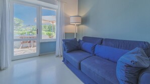 Une pièce avec un canapé bleu, une lampe et une vue sur une terrasse extérieure avec une table et des chaises.