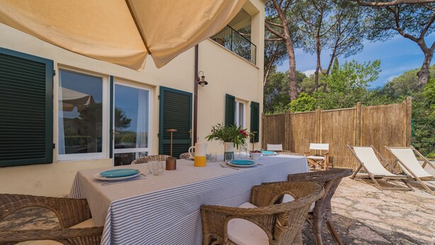 Un espace extérieur aménagé pour les repas, avec une table pour deux, des chaises en osier et une vue sur une clôture en bois et des arbres.