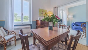 Un coin repas avec une table et des chaises en bois, un vase rempli de fleurs et une vue sur la verdure à l’extérieur.