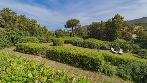 Un jardin luxuriant, avec des haies soigneusement taillées, une grande variété d’arbres et une vue dégagée sur la mer en arrière-plan.