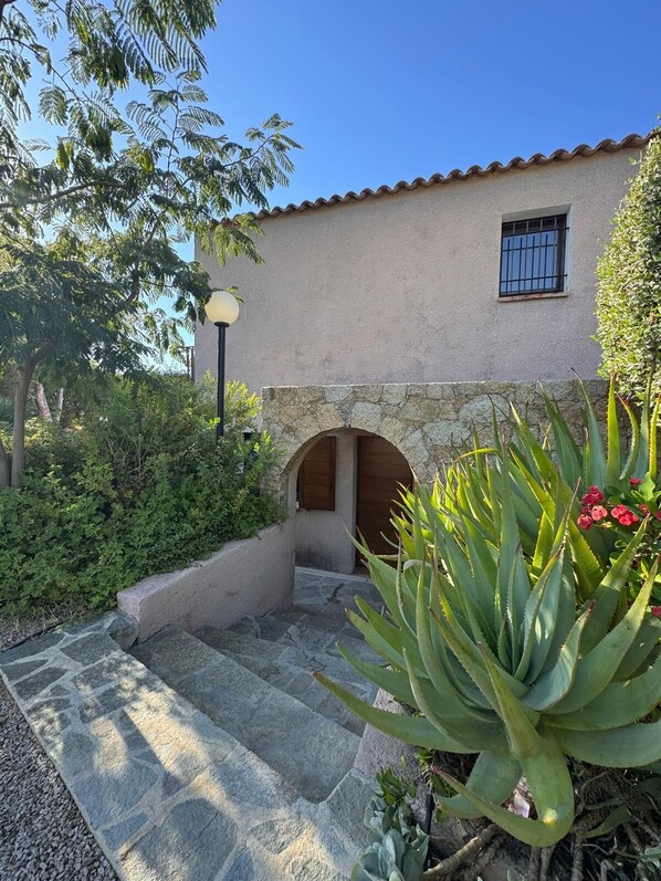 Un edificio con una entrada de arco de piedra, rodeado de follaje y una planta de aloe grande.