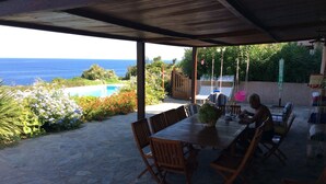 A covered patio with stone flooring, wooden furniture, and a view of the ocean. - WONDERFUL VILLA ON THE SEA 8/10 PEOPLE  (Lumio)