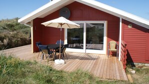 Une cabane en bois rouge avec une terrasse, une table et des chaises, et un grand parasol.