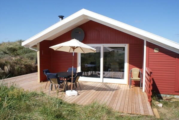 A red wooden cabin with a deck, a table with chairs, and a large umbrella.