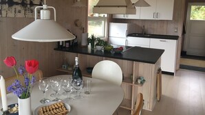Une cuisine moderne avec des armoires blanches, un comptoir noir et des luminaires suspendus. On y trouve une table à manger ornée d’un vase de fleurs et d’une assiette de collations.