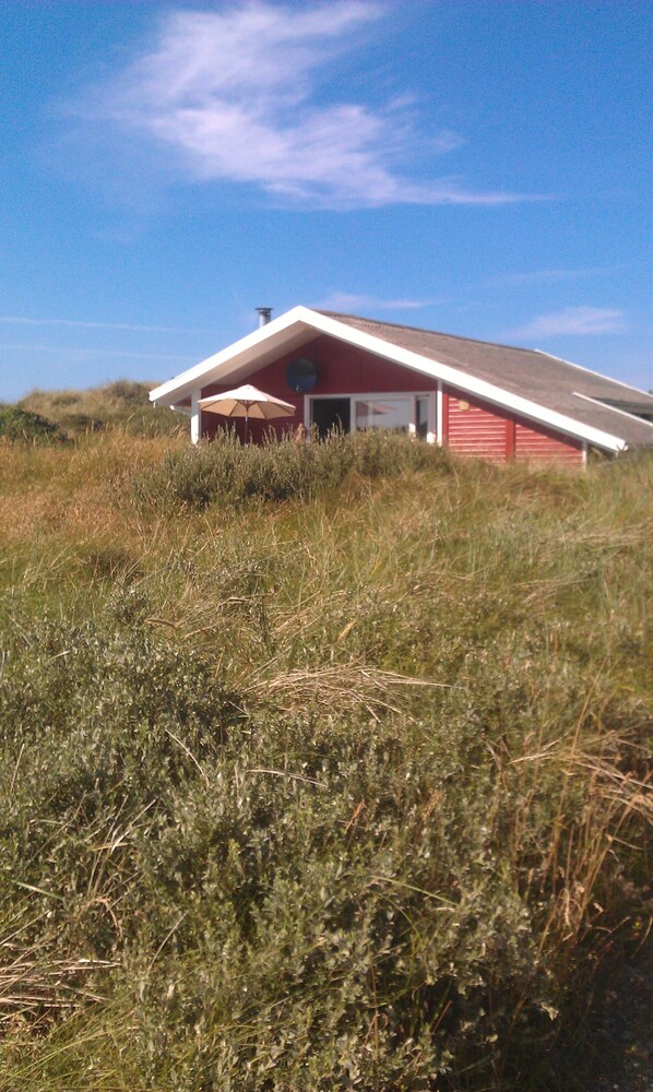 Un bâtiment rouge avec un toit blanc, entouré d’herbe haute.