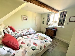 Ein Schlafzimmer mit zwei Einzelbetten, einem Nachttisch mit Spiegel, einer Kommode und einem Fenster mit Vorhängen.