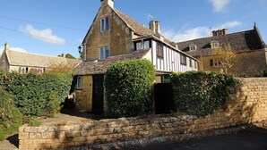 Une maison traditionnelle en pierre, dotée d’un toit à forte pente, d’une cheminée et d’un petit abri attenant.