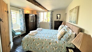 Une chambre à coucher avec un lit, une commode, une fenêtre avec des rideaux, un radiateur et un tableau accroché au mur.
