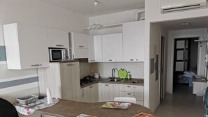 A modern kitchen with white cabinets, a microwave, and a green apple-shaped cutting board. - TWO-ROOM APARTMENT NEW SEA VIEW GALLINARA ISLAND DIRECTLY ON THE BEACH (ALBENGA)