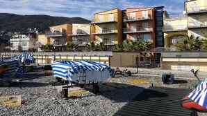 A coastal area with multi-story buildings, some with balconies, and a beach with covered beach chairs. - TWO-ROOM APARTMENT NEW SEA VIEW GALLINARA ISLAND DIRECTLY ON THE BEACH (ALBENGA)