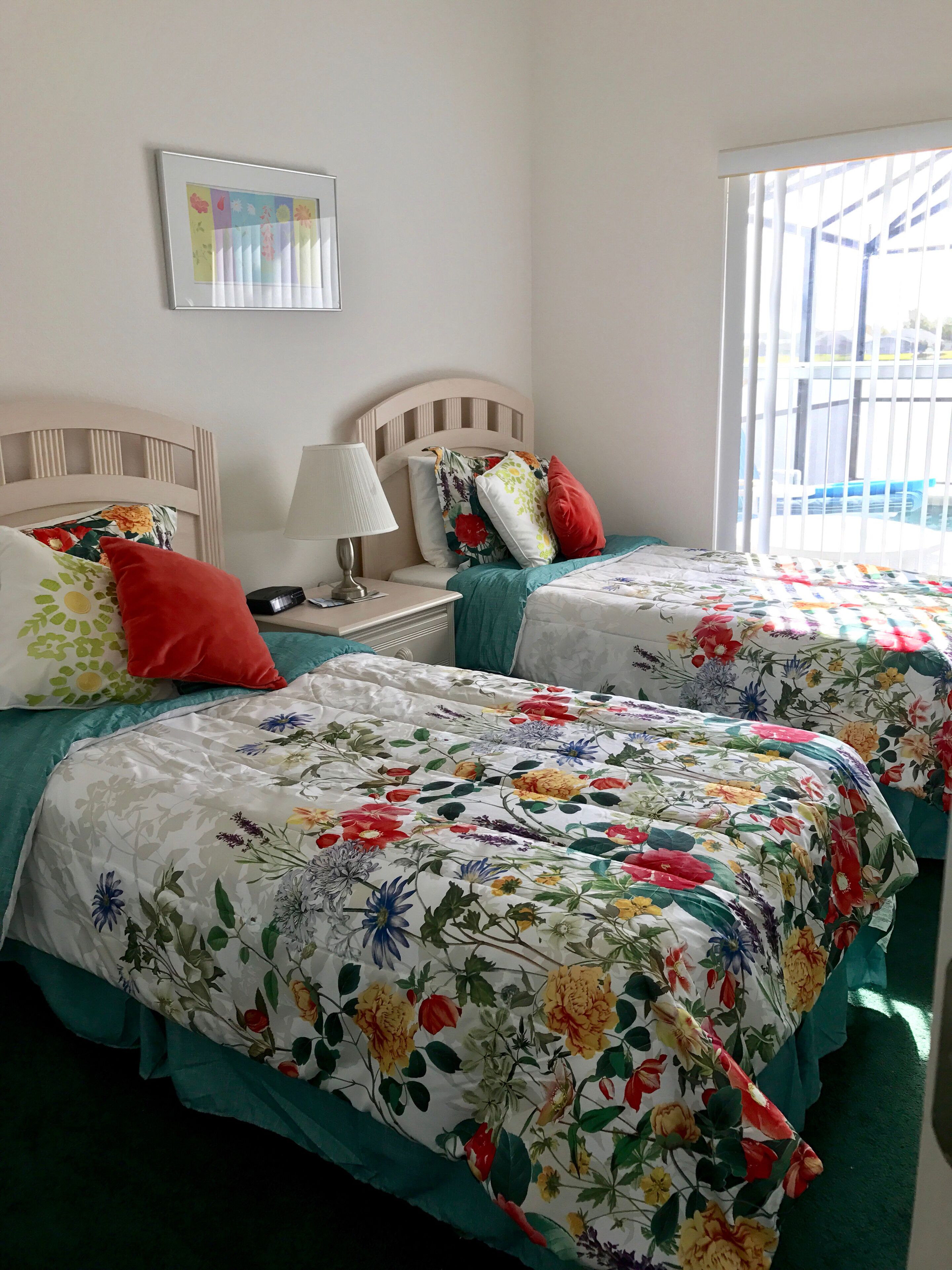 Una habitació amb dos llits, cadascun amb roba de llit floral i un capçal. Hi ha una tauleta de nit amb una làmpada i una fotografia emmarcada a la paret.
