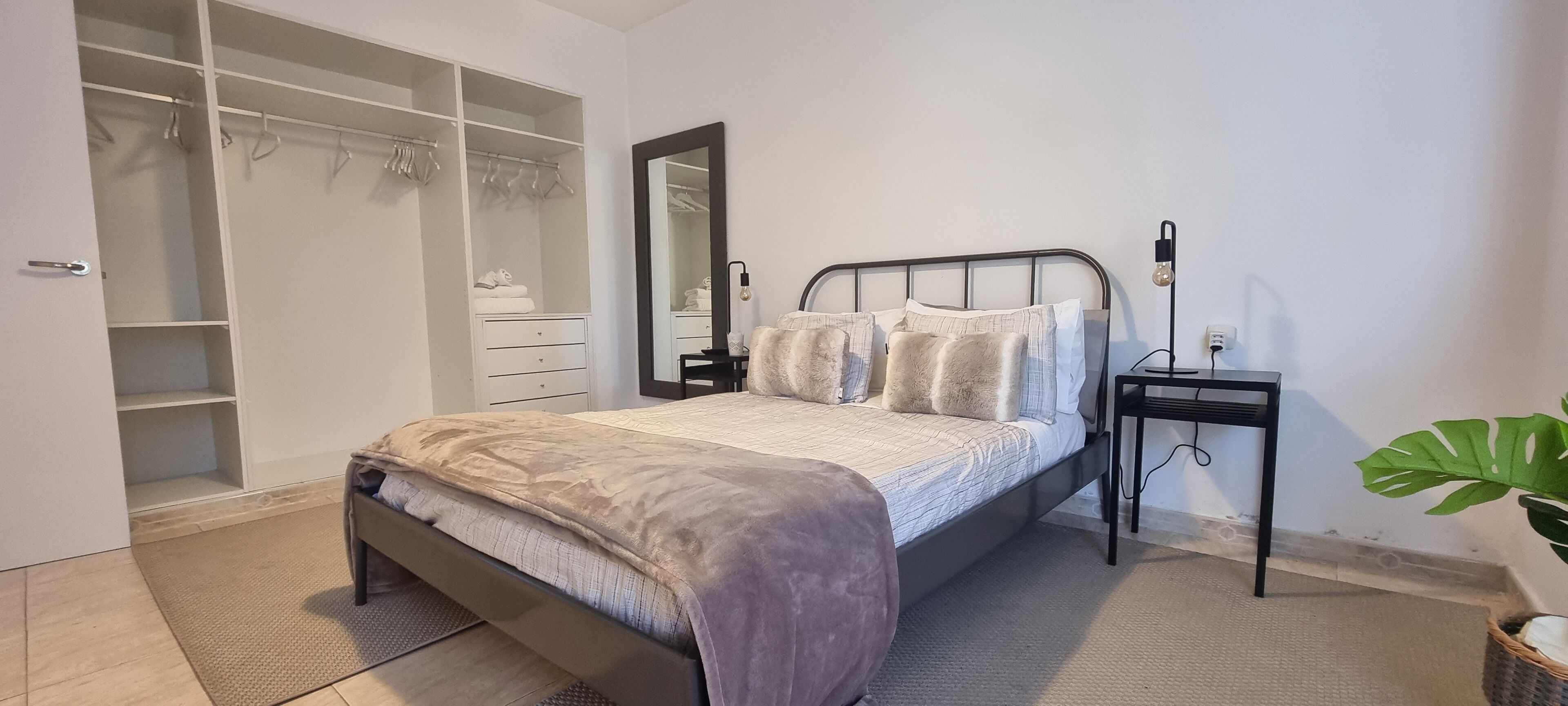 Ein Schlafzimmer mit Bett, Nachttisch, Kleiderschrank und einem großen Spiegel.