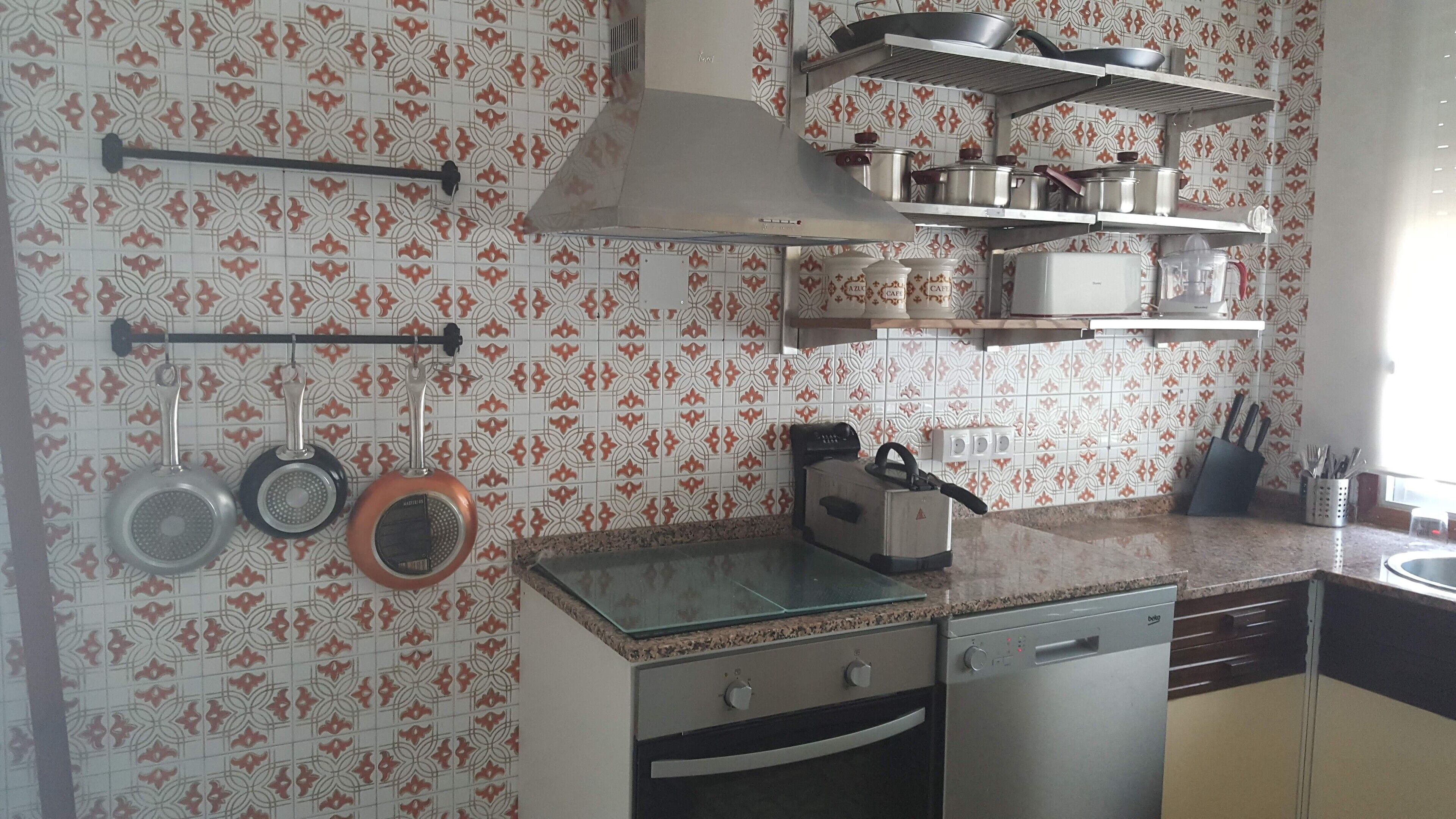 Una cocina con baldosas estampadas, ollas colgantes, una estufa y un lavavajillas.