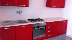 A kitchen with red cabinets, a stainless steel sink, a gas stove, and a built-in oven. - studio - 1 room - 3/4 persons (Torre Delle Stelle)
