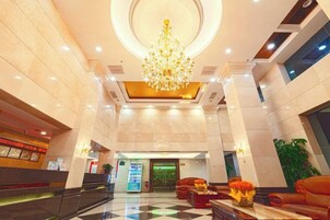 A hotel lobby with a chandelier, reception desk, and seating area.