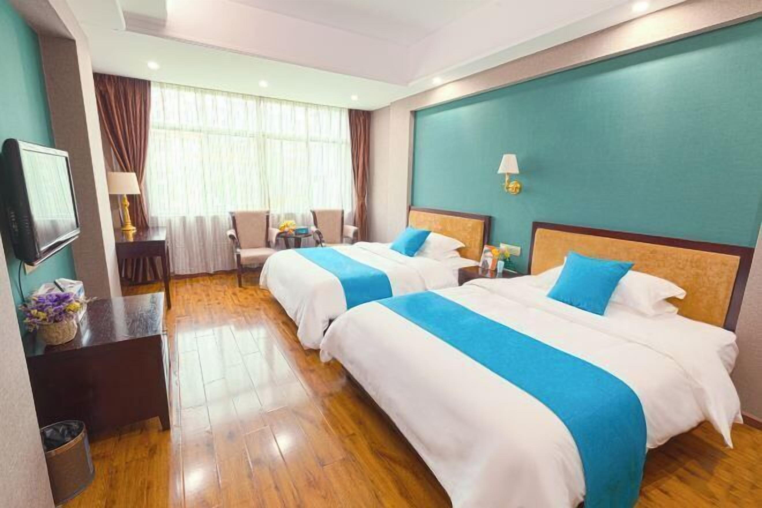Habitación de hotel con dos camas, televisión, escritorio y ventana con cortinas.