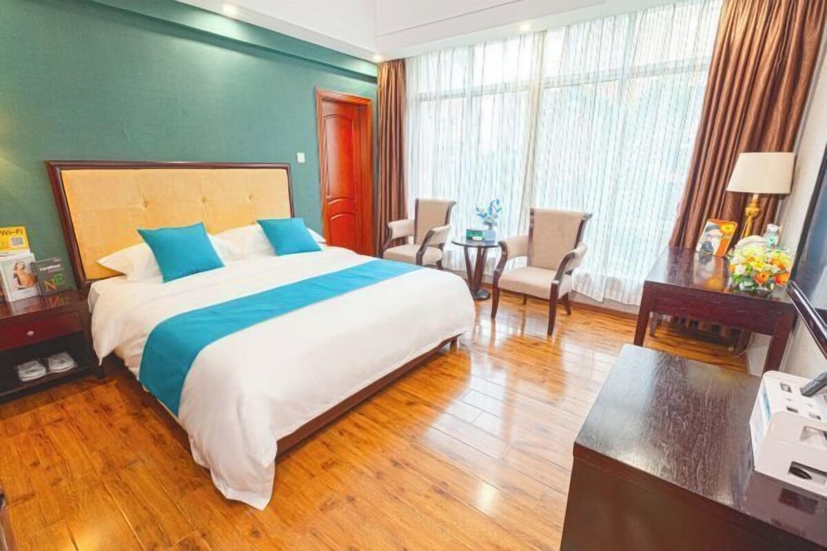 A hotel room with a large bed, two chairs, a desk, and a window with curtains.