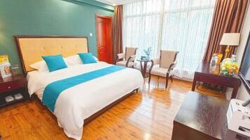 A hotel room with a large bed, two chairs, a desk, and a window with curtains.