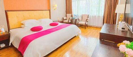 A hotel room with a large bed, a desk, a chair, and a TV.