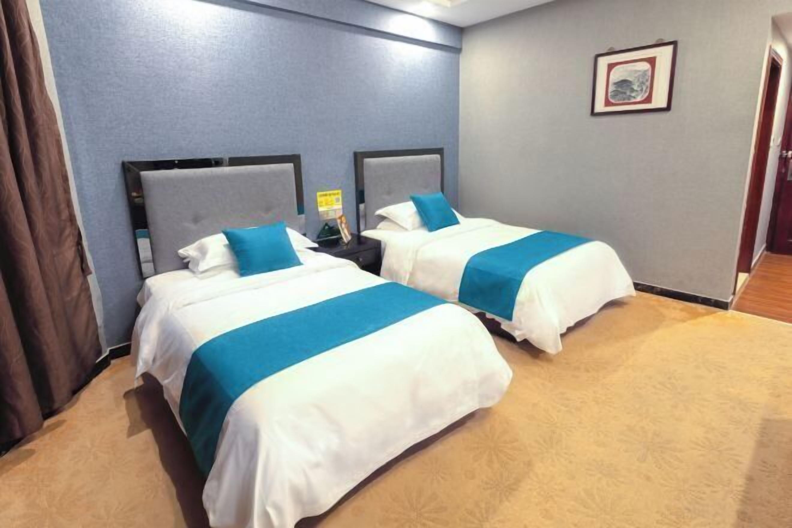 Habitación de hotel con dos camas, cada una con cabecero y colcha azul y blanca.