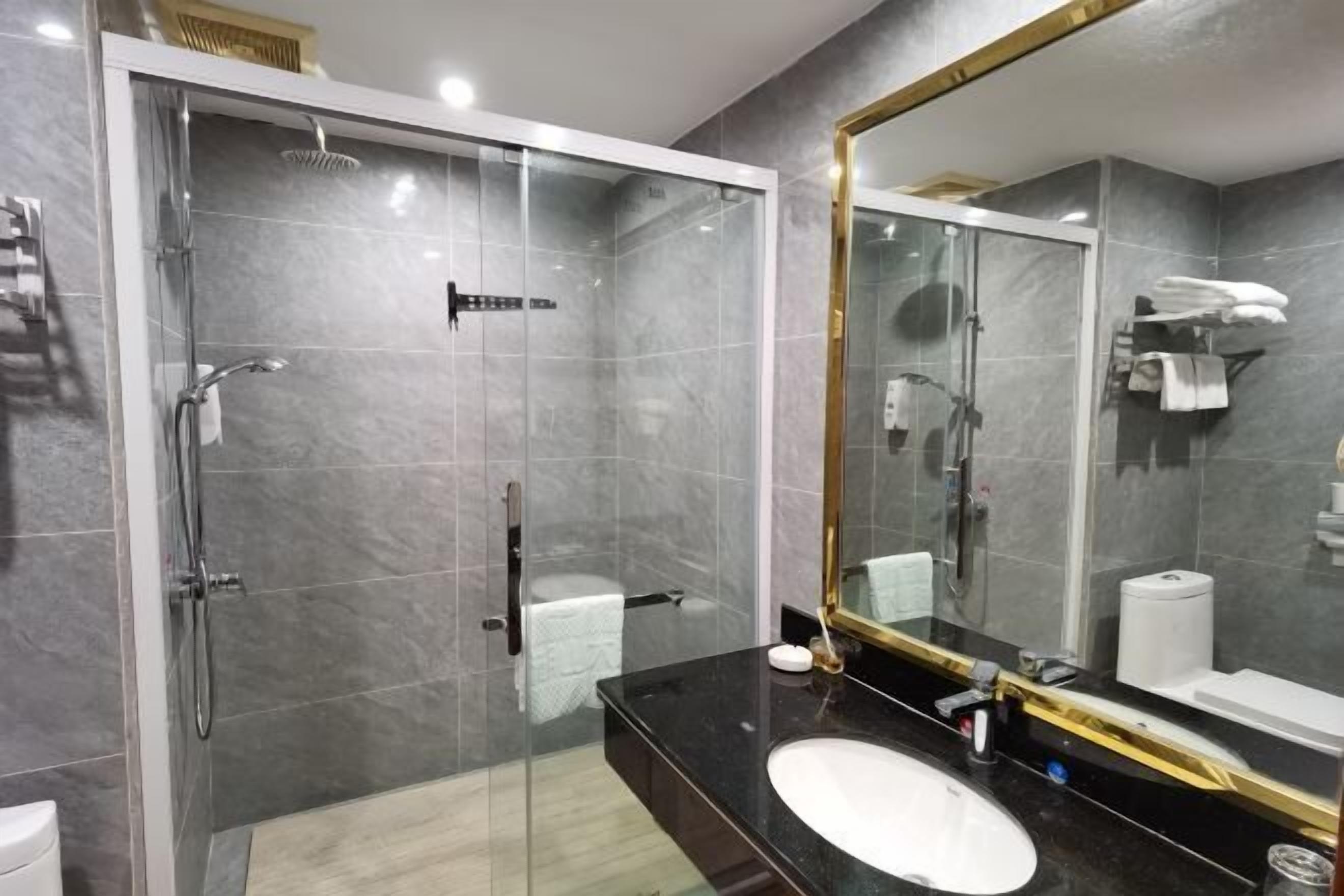 Un baño moderno con ducha de vidrio, un espejo grande y un lavabo de mármol negro.