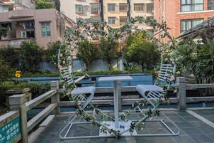 Terraza en la azotea con una mesa y sillas de metal, rodeada de vegetación y vistas a edificios residenciales.