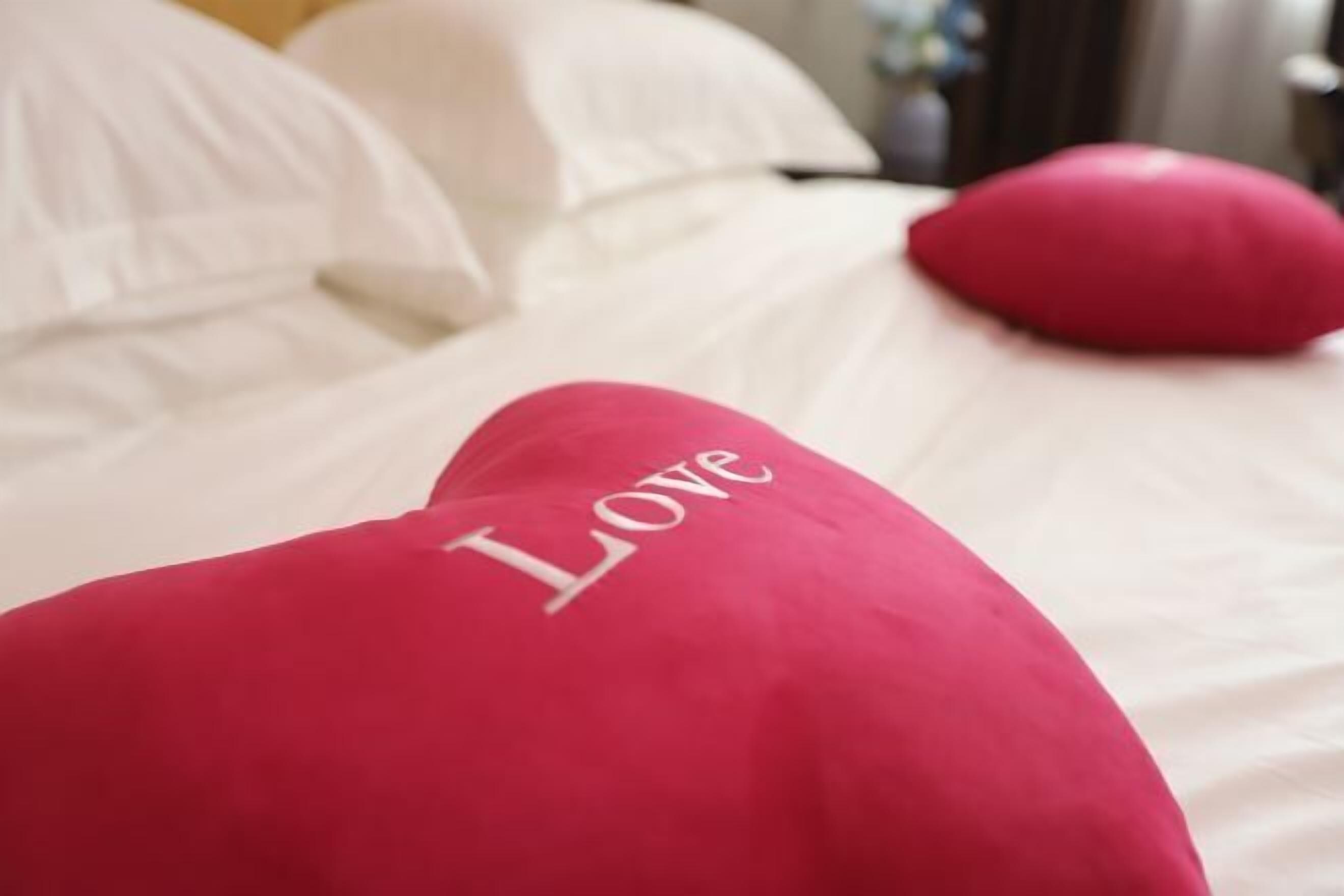 A bed with white bedding and a red pillow with the word "LOVE" on it.