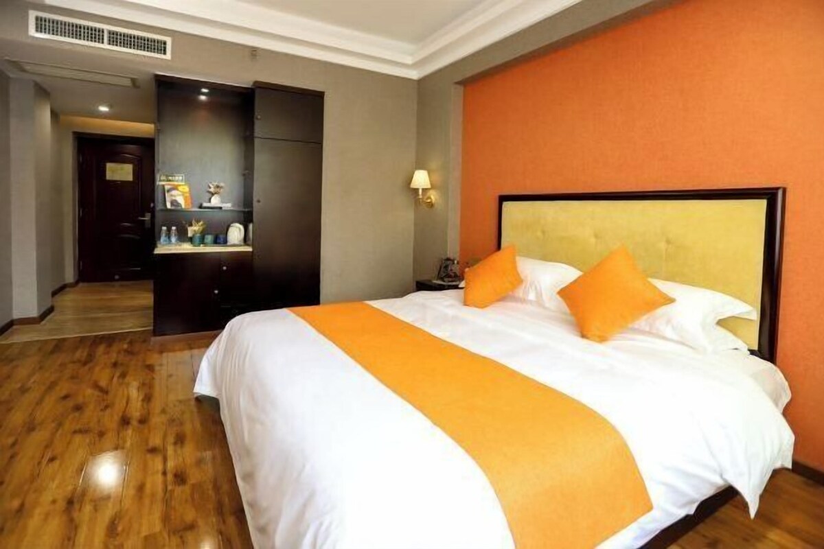 A hotel room with a large bed, a wooden floor, a dark wardrobe, and a wall-mounted lamp.