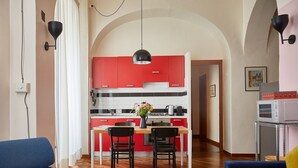 A modern kitchen with red cabinets, a central island, and a dining area with two chairs. - TrastevereHome - Garibaldi Rome (Roma)