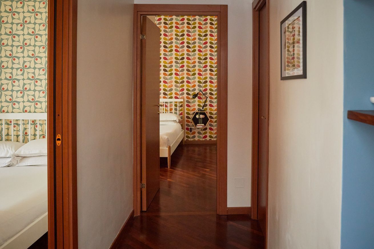 A narrow hallway leading to a bedroom with a bed, a nightstand, and a lamp.
