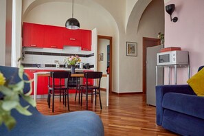 Een moderne keuken met rode kastjes, een eethoek met stoelen, een blauwe bank en een magnetron op een standaard.