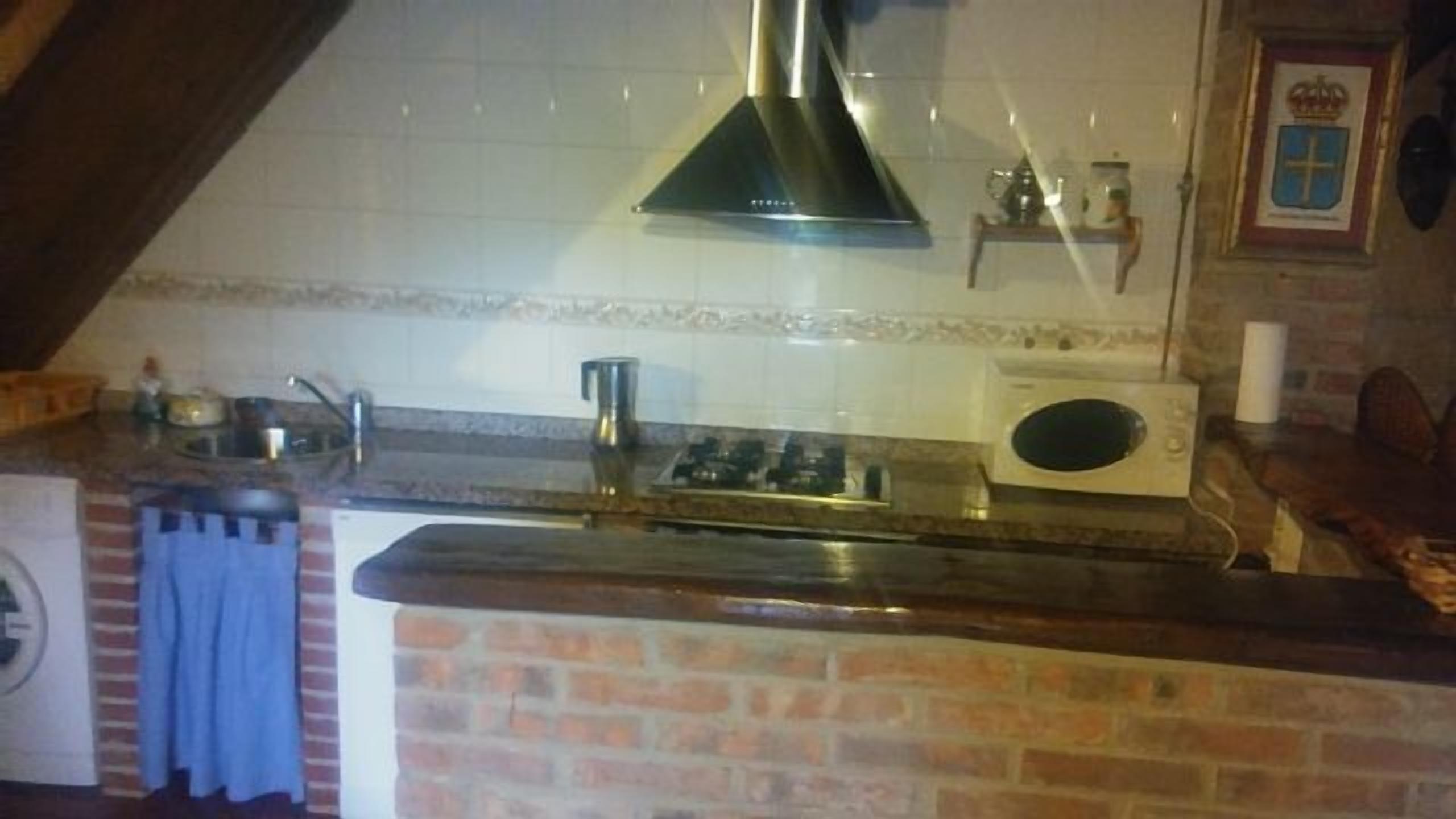A kitchen with a brick wall, a stainless steel range hood, a kettle, and a microwave.