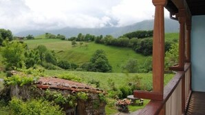 Un edificio rústico de piedra con tejado de tejas, un balcón de madera y vistas a un valle verde exuberante.