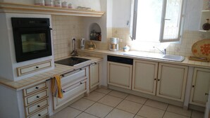 Une cuisine avec des meubles blancs, une cuisinière, un évier et une fenêtre.