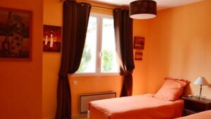 Une chambre avec deux lits, des murs orange, une fenêtre avec des rideaux et une lampe sur une table de chevet.