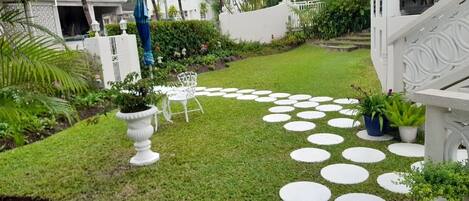 Un jardí ben cuidat amb un dibuix circular de pedres per a camí, una zona d'estar exterior blanca i vegetació abundant.