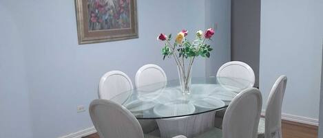 A dining area with a glass table surrounded by white chairs, a vase with flowers, and a ceiling fan.