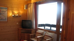 Een gezellig houten interieur met wanden van hout, een televisie op een houten standaard, een tafeltje met twee rode vazen en twee comfortabele stoelen.