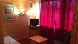 Een gezellige kamer met een bed, een klein houten tafeltje, een televisie en een stoel.