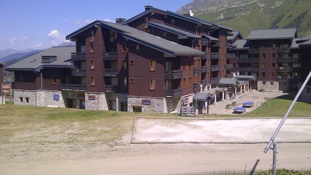 Een hotel met meerdere verdiepingen, balkons, stenen fundamenten en een achtergrond van een wintersportgebied.