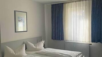A hotel room with two beds, a ceiling light, a window with curtains, and a framed picture on the wall.