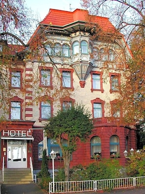 Il s’agit d’un bâtiment historique à la façade en briques rouges, doté de nombreuses fenêtres et d’une enseigne indiquant qu’il s’agit d’un hôtel.