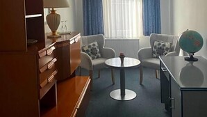 A hotel room with a desk, two chairs, a round table, a globe, and a window with curtains.