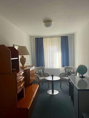 Une chambre d’hôtel équipée d’un bureau, de deux chaises, d’une table ronde, d’un globe terrestre et d’une fenêtre avec des rideaux.