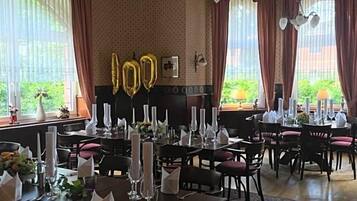 A dining area with tables set for a meal, large windows with curtains, and a chandelier.