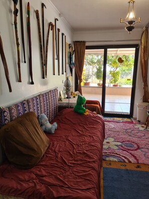 A bedroom with a bed, pillows, a stuffed toy, a lamp, a window with curtains, and a view of the outside.