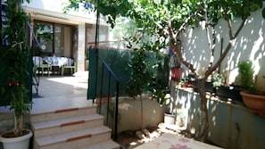 A staircase leading to a covered outdoor area with a table and chairs, surrounded by potted plants and a wall with a climbing plant.