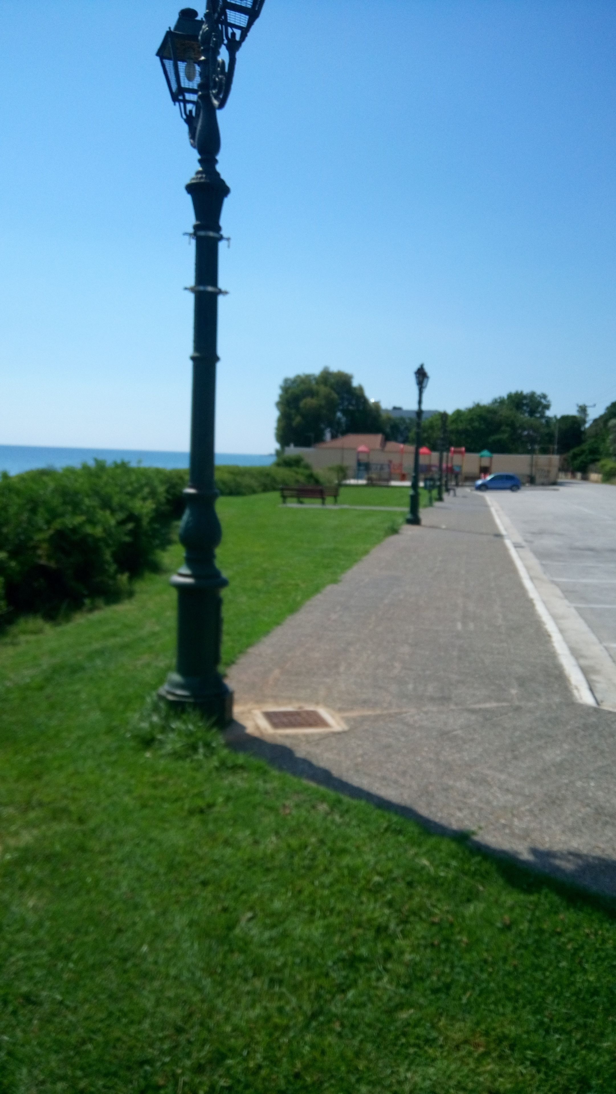 Eine Straße mit einem grünen Laternenpfahl, einem Bürgersteig und einem Gebäude im Hintergrund.